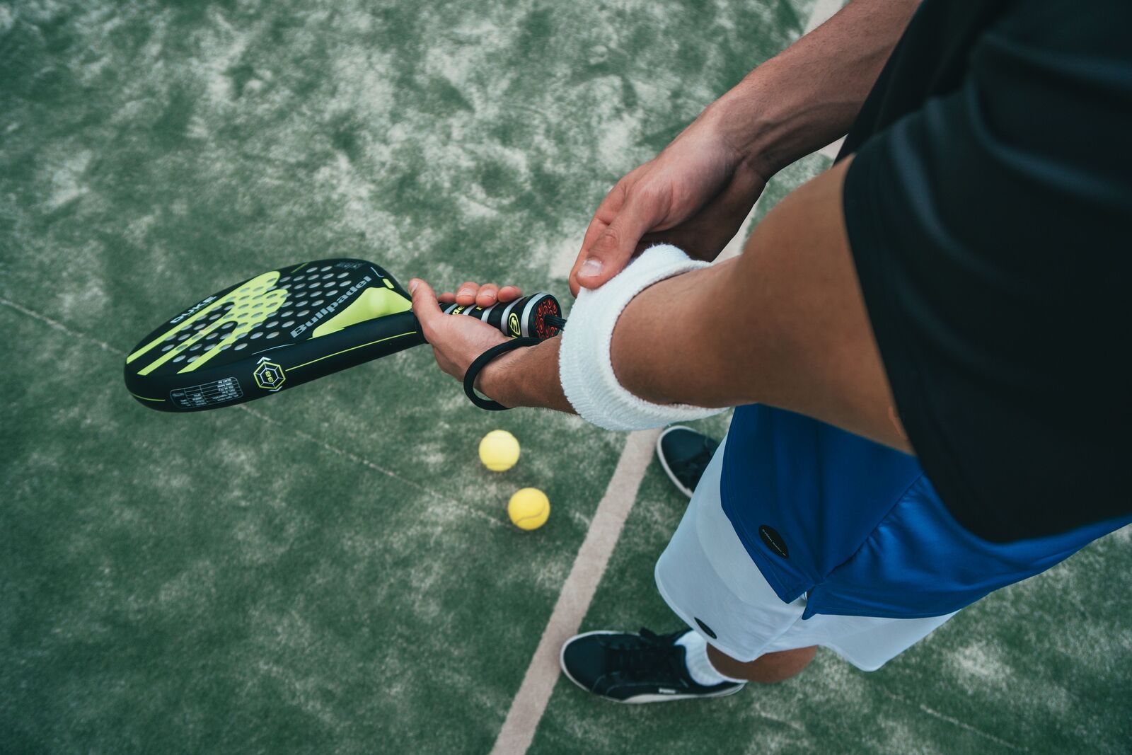 Primer plano de un jugador de pádel con la pala en la mano y pelotas sobre la pista