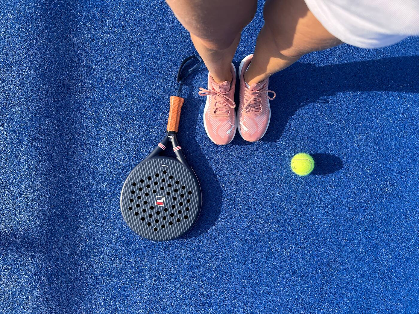 Pala, pelota y zapatillas sobre una pista de pádel azul